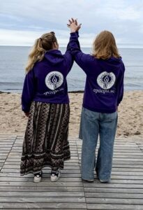 Bilden visar 2 barnledare som står vid strandkanten med ryggen mot kameran. De håller varandra i hand högt över huvudet. På sig har de lila tröjor med epilepsiförbundets logotype.